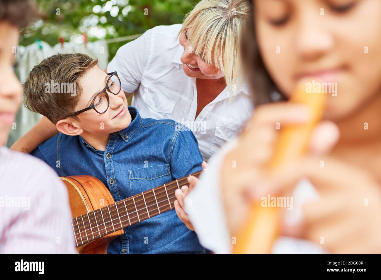 Lehrer hilft Kind mit Gitarre während Musikunterricht im Sommer Camp oder Sommercamp Stockfoto
