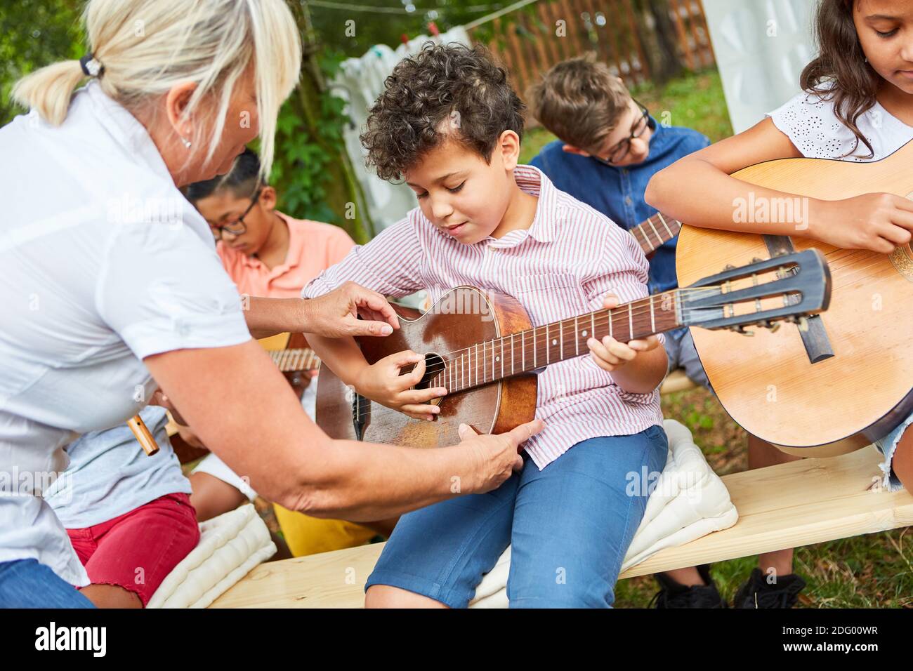 Lehrer hilft Kind, Gitarre in der Musikklasse zu lernen Im Sommerlager Stockfoto