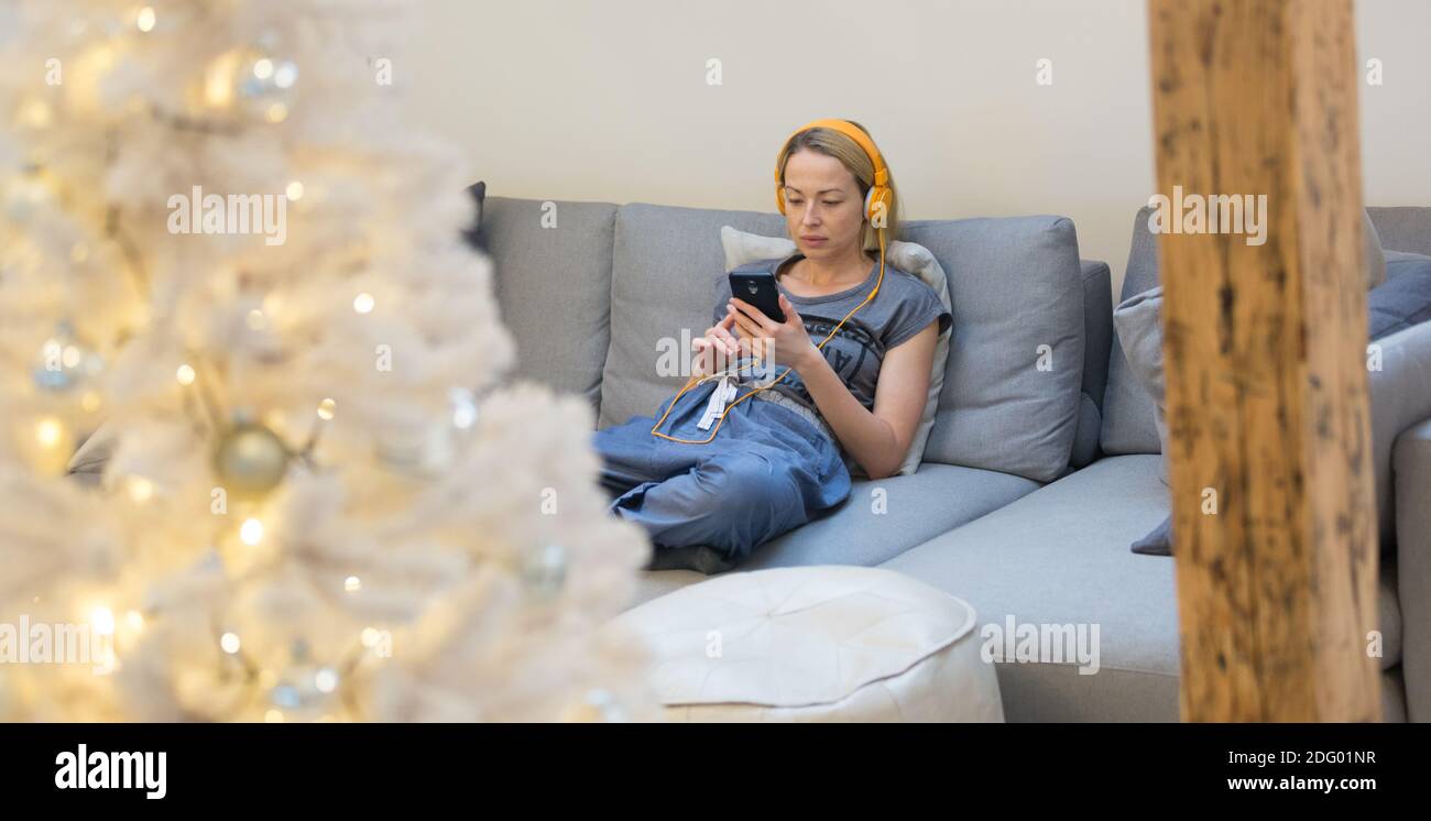 Junge nachdenkliche Frau sitzt drinnen zu Hause Wohnzimmer Sofa Nutzung sozialer Medien am Telefon für Videochats und Aufenthalte Verbunden mit ihr geliebt Stockfoto