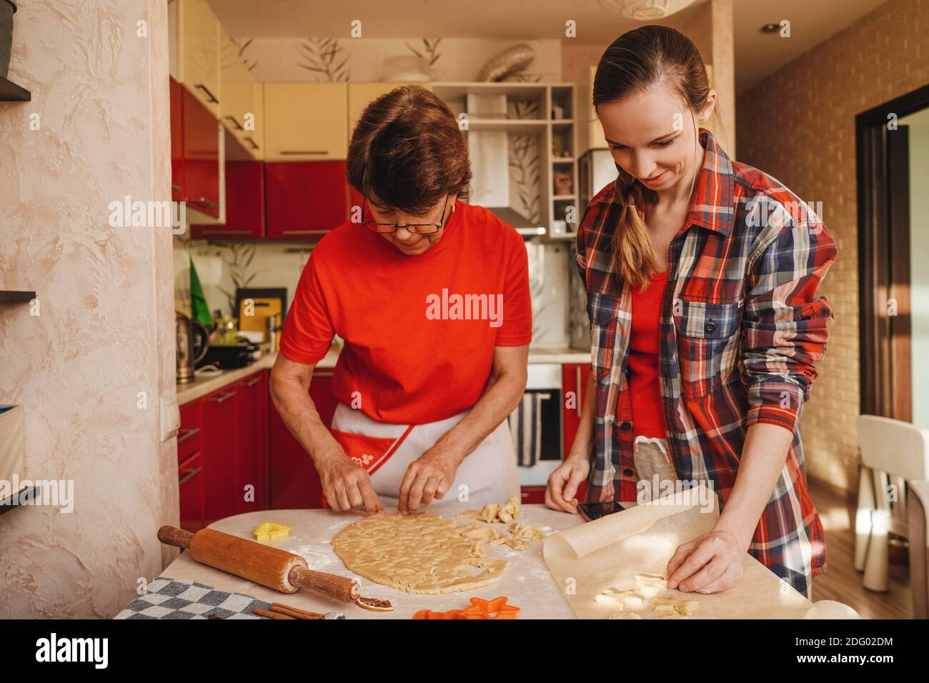 Junge Frau und ältere Mutter kochen Kekse in roten Kleidern. Stockfoto