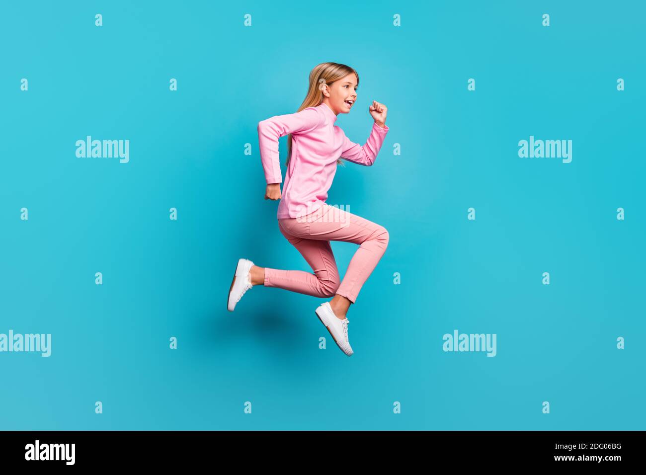 Profil in voller Länge Foto von niedlichen positiven Teenager-Mädchen springen Tragen rosa Hosen Poloneck weißen Schuhe isoliert auf blauem Hintergrund Stockfoto