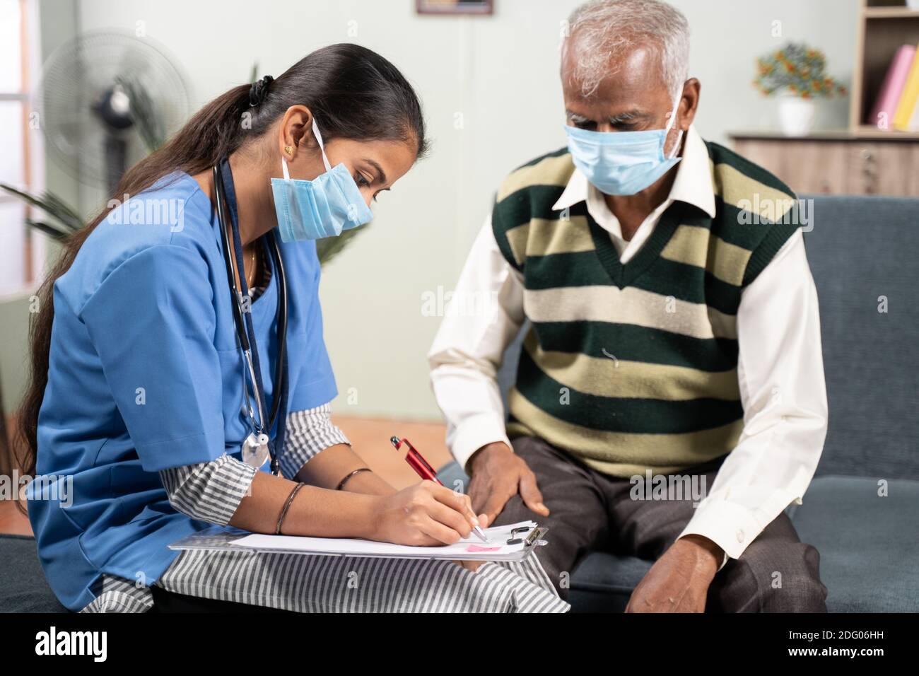 Junge Arzt oder Krankenschwester schreiben Rezept während des Hausbesuches zu Kranker älterer Mann, während beide Gesichtsmaske getragen wegen Coronavirus covid-19 Pandemie Stockfoto