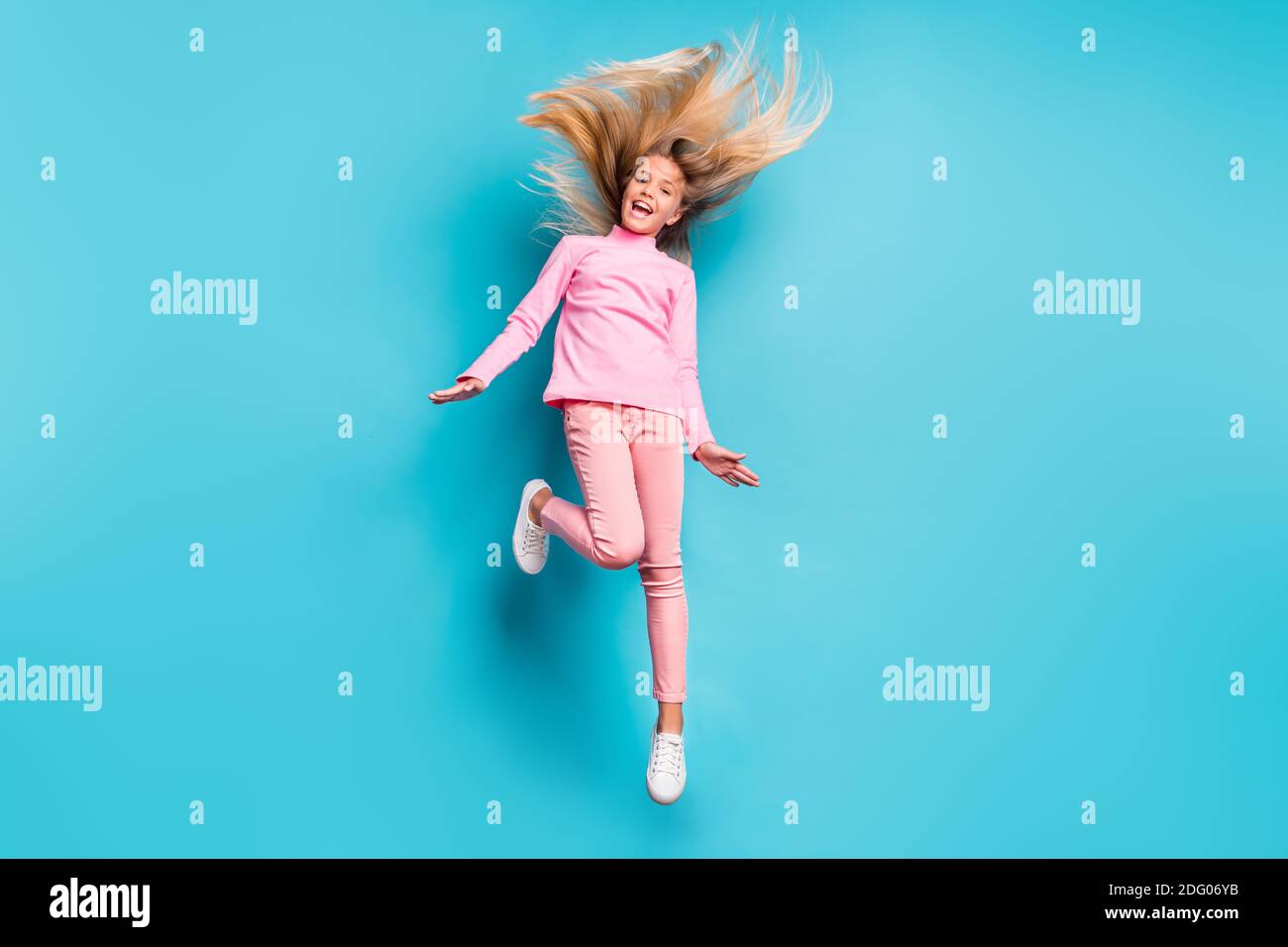 Foto in voller Größe von erstaunt positive Teenager-Mädchen springen Haare Up tragen rosa Hose Poloneck weiß Schuhe isoliert auf teal Hintergrund Stockfoto