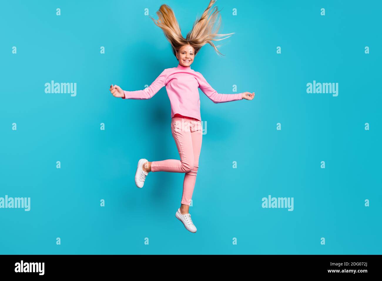 Foto in voller Größe von lustigen positiven Teenager springen Haare nach oben Tragen Sie rosa Hosen Poloneck weißen Schuhe isoliert auf blauem Hintergrund Stockfoto