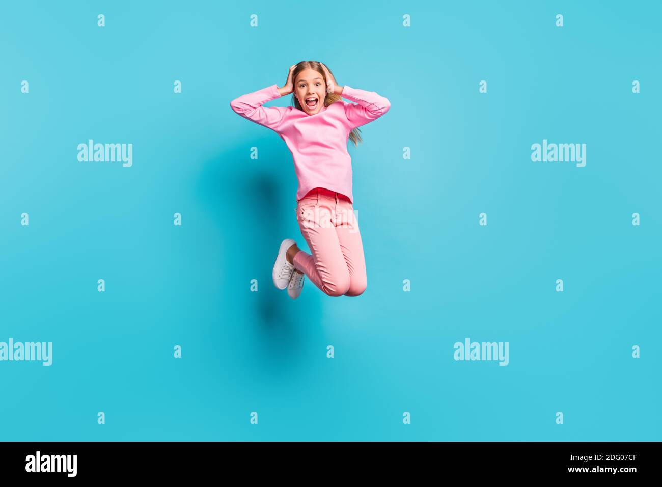 In voller Größe Foto von cool überrascht ziemlich teen Mädchen springen Air Hände Kopf schreien tragen rosa Hosen Poloneck weißen Schuhen Isoliert auf blauem Hintergrund Stockfoto