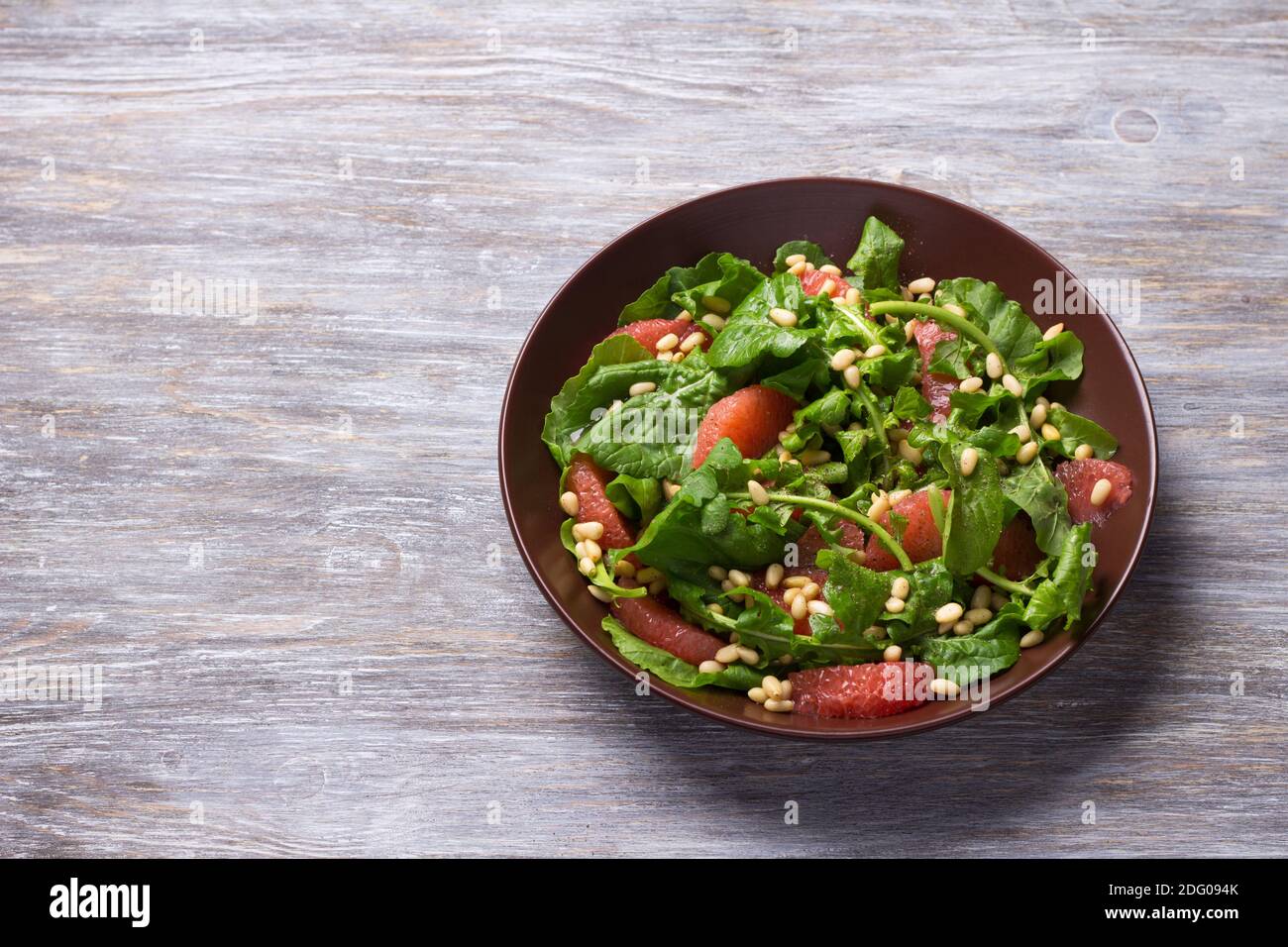 Frischer Salat aus Rucola mit Grapefruit und Pinienkernen auf Holzgrund, freier Platz. Gesundes, leckeres Essen Stockfoto