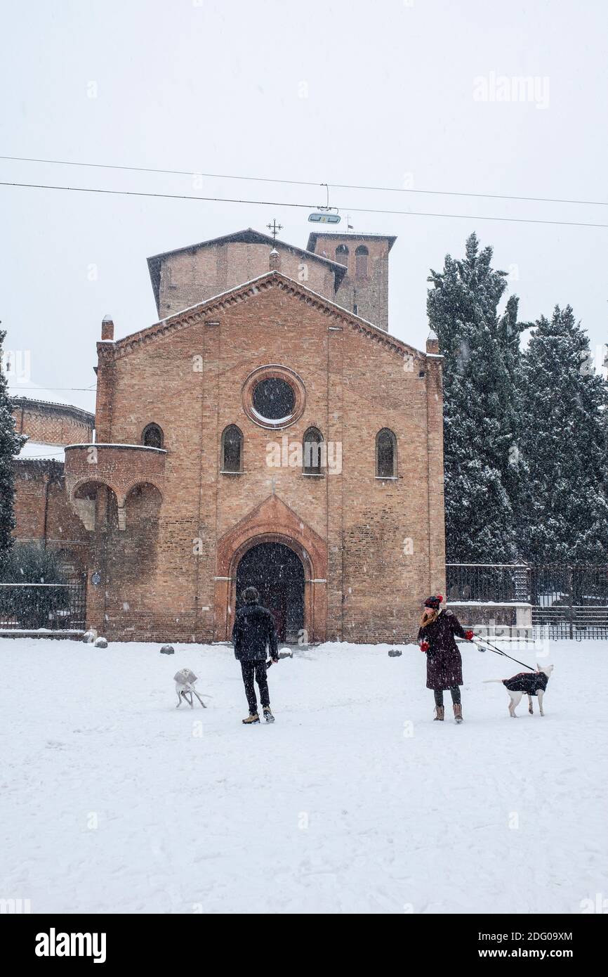 Menschen mit Hunden im fallenden Schnee außerhalb der Basilika di Santo Stefano, Bologna, Italien. Stockfoto