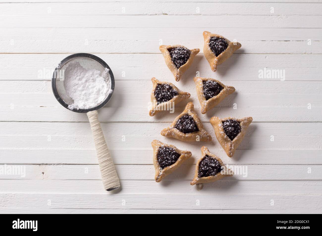 Traditionelle Süßigkeiten für den jüdischen Feiertag Purim. Hamantashen Plätzchen oder Ohren von Haman, dreieckige Plätzchen mit Mohn und Rosinen auf weißem Rücken Stockfoto