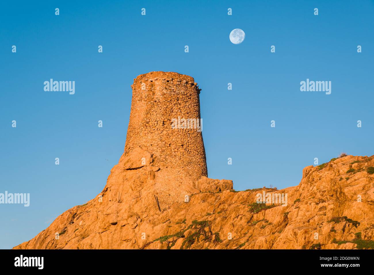 Der Mond erscheint hinter dem alten genuesischen Turm bei La Pietra, dem roten Felsen, bei Ile Rousse in der Balagne-Region von Korsika Stockfoto