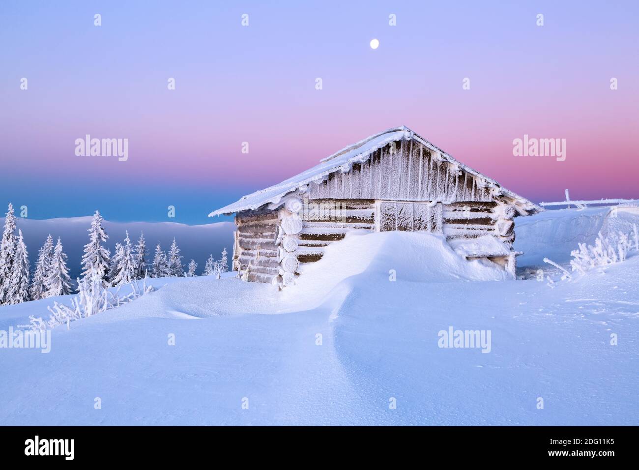 Winterlandschaft. Toller Sonnenaufgang. Alte Holzhütte auf der Wiese mit Schnee bedeckt. Landschaft von hohen Bergen und Wäldern. Hintergrund des Hintergrundbilds. Lage Stockfoto