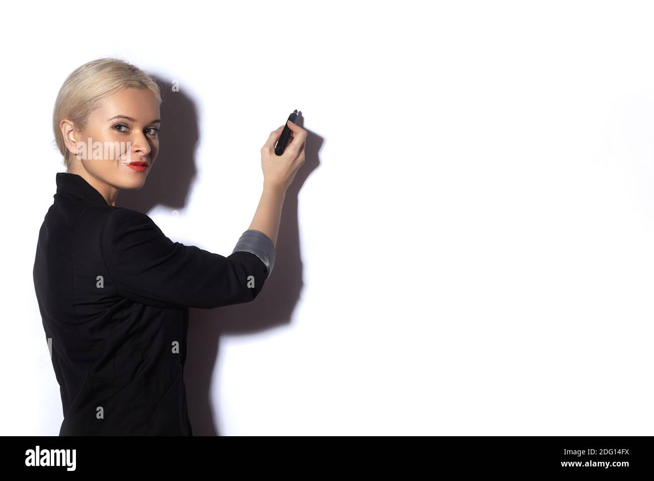 Hübsche Geschäftsfrau, die Notizen auf einem reflektierenden Brett schreibt. Modischer Bürostil. Blonde Modell Präsentation mit Marker auf weiß Stockfoto