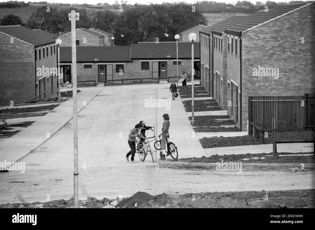 70er Jahre England Neustadt in Entwicklung, Häuser gebaut, aber nicht alle Arbeiten noch fertig, Gärten nicht gepflanzt, aber neue Bewohner haben und ziehen in. Kinder, die auf ihren Fahrrädern in der leeren Straße spielen 1977 HOMER SYKES Stockfoto