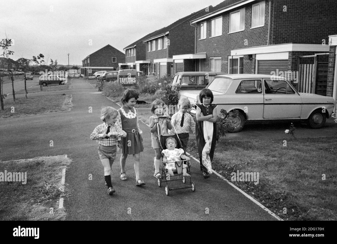 Kinder aus den 70er Jahren Großbritannien. Eine Gruppe von kleinen Kindern, die zu den Geschäften gehen und die kleine Schwester in ihren Kinderwagen schieben. Sie sind sehr elegant gekleidet, leben in einer modernen Wohnsiedlung England 1977 HOMER SYKES Stockfoto