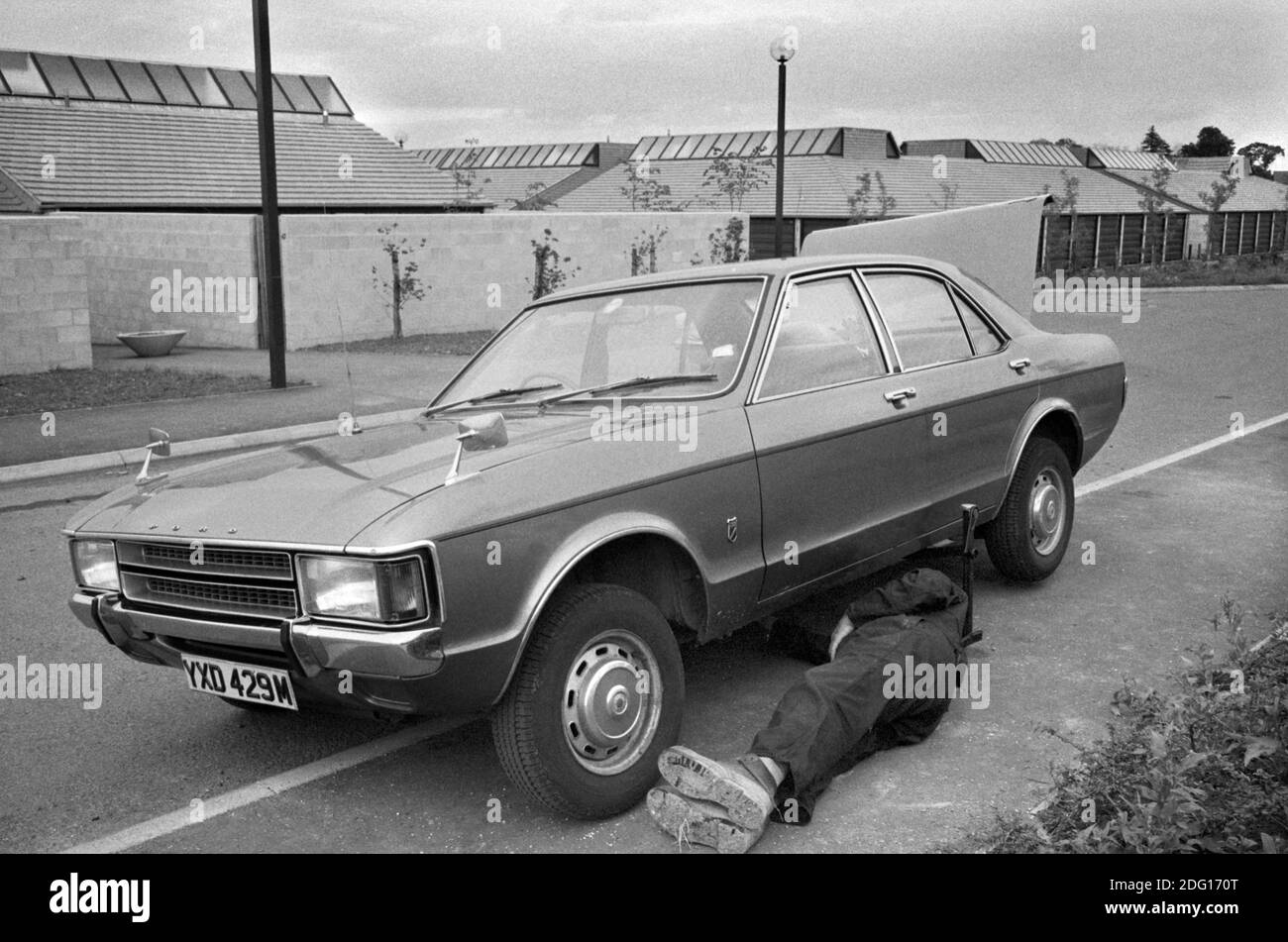 Milton Keynes New Town 1970er Jahre Mann, der am Straßenrand an seinem Auto arbeitete und einige Reparaturen durchführte. Moderne Wohnsiedlung 1977 UK Milton Keynes, Buckinghamshire HOMER SYKES Stockfoto