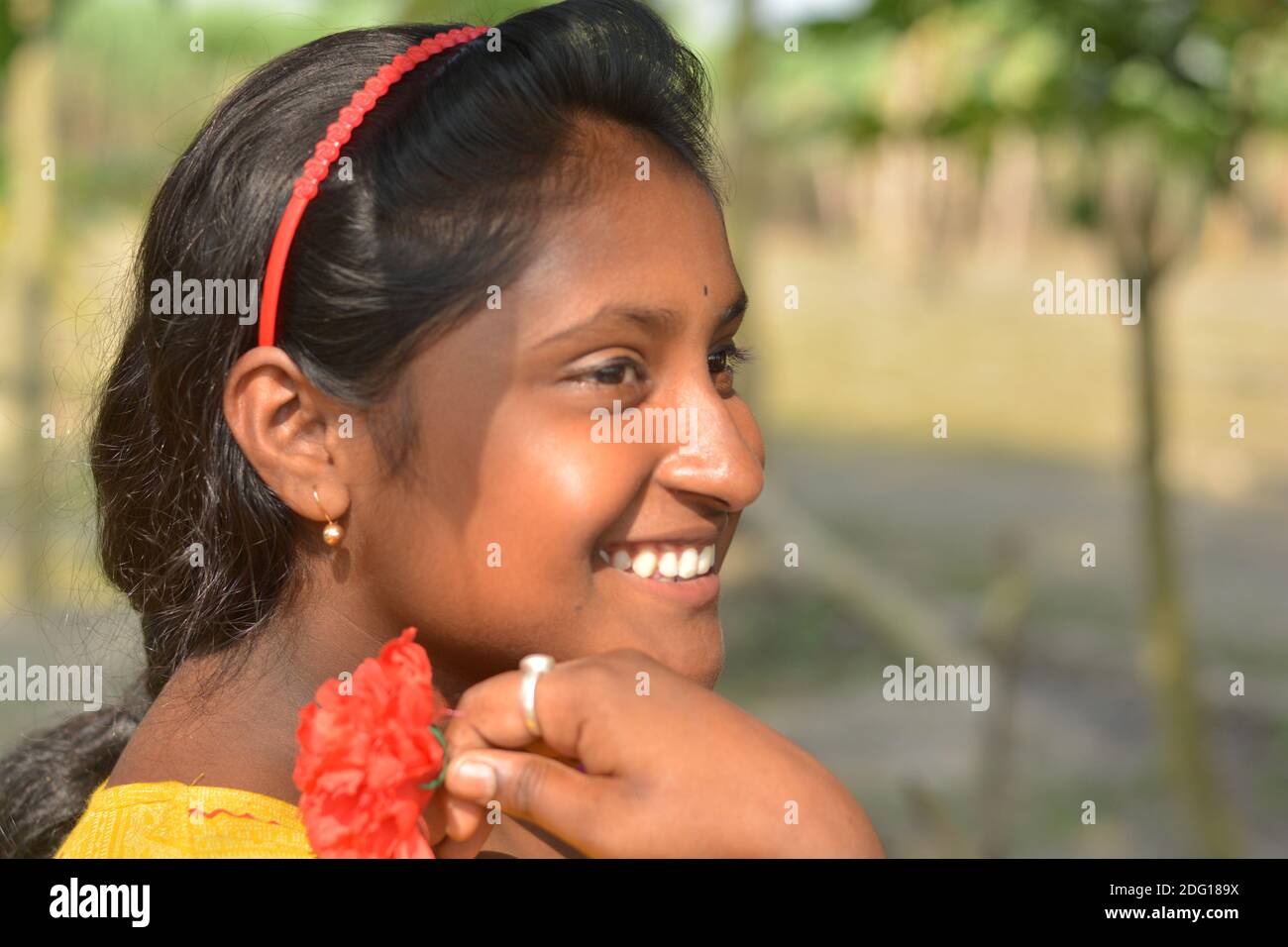 Nahaufnahme eines indischen Dorf Teenager-Mädchen lächelnd mit Blume in der Hand und trägt Haarband und Gold Ohrring Stockfoto