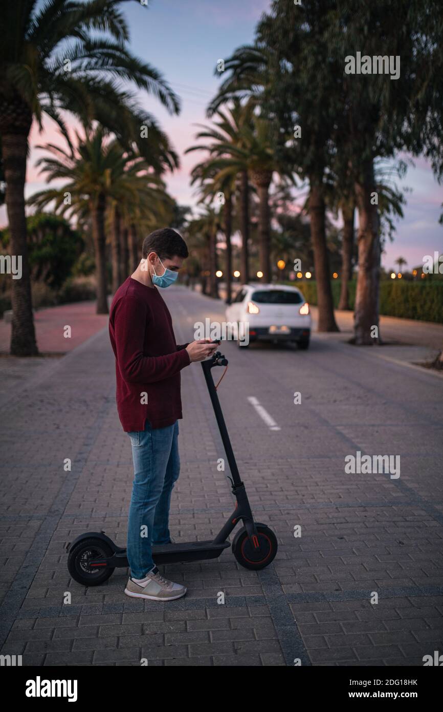Junger Mann steht mit seinem E-Scooter auf der Straße, um die Straße zu überqueren. Konzepttechnologie. Stockfoto