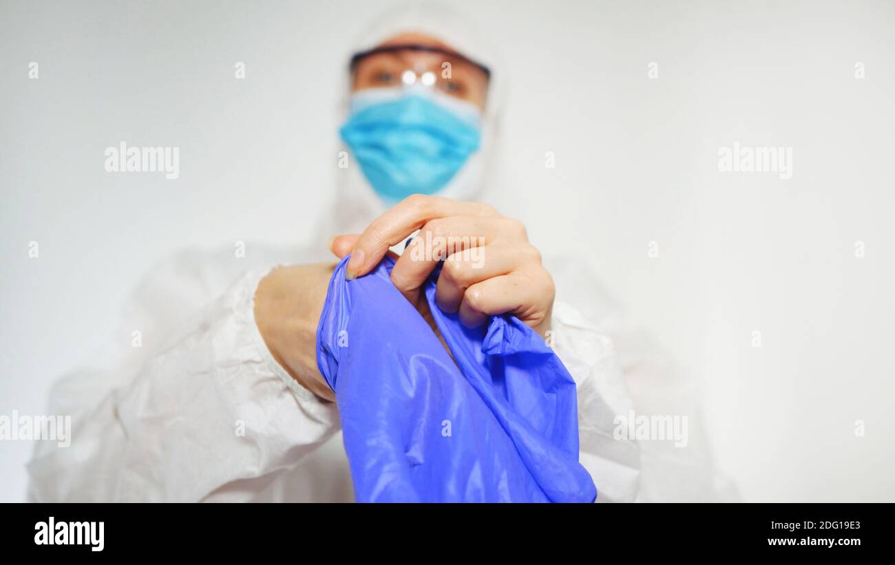 Der Arzt im Schutzanzug zieht Handschuhe an. Stockfoto
