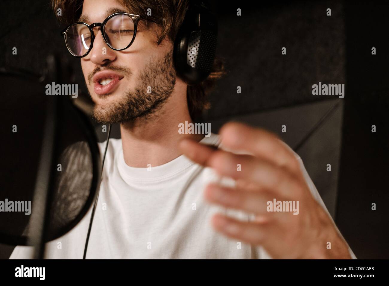 Nahaufnahme junger männlicher Sänger in Kopfhörern, der emotional einsingt Tonstudio Stockfoto