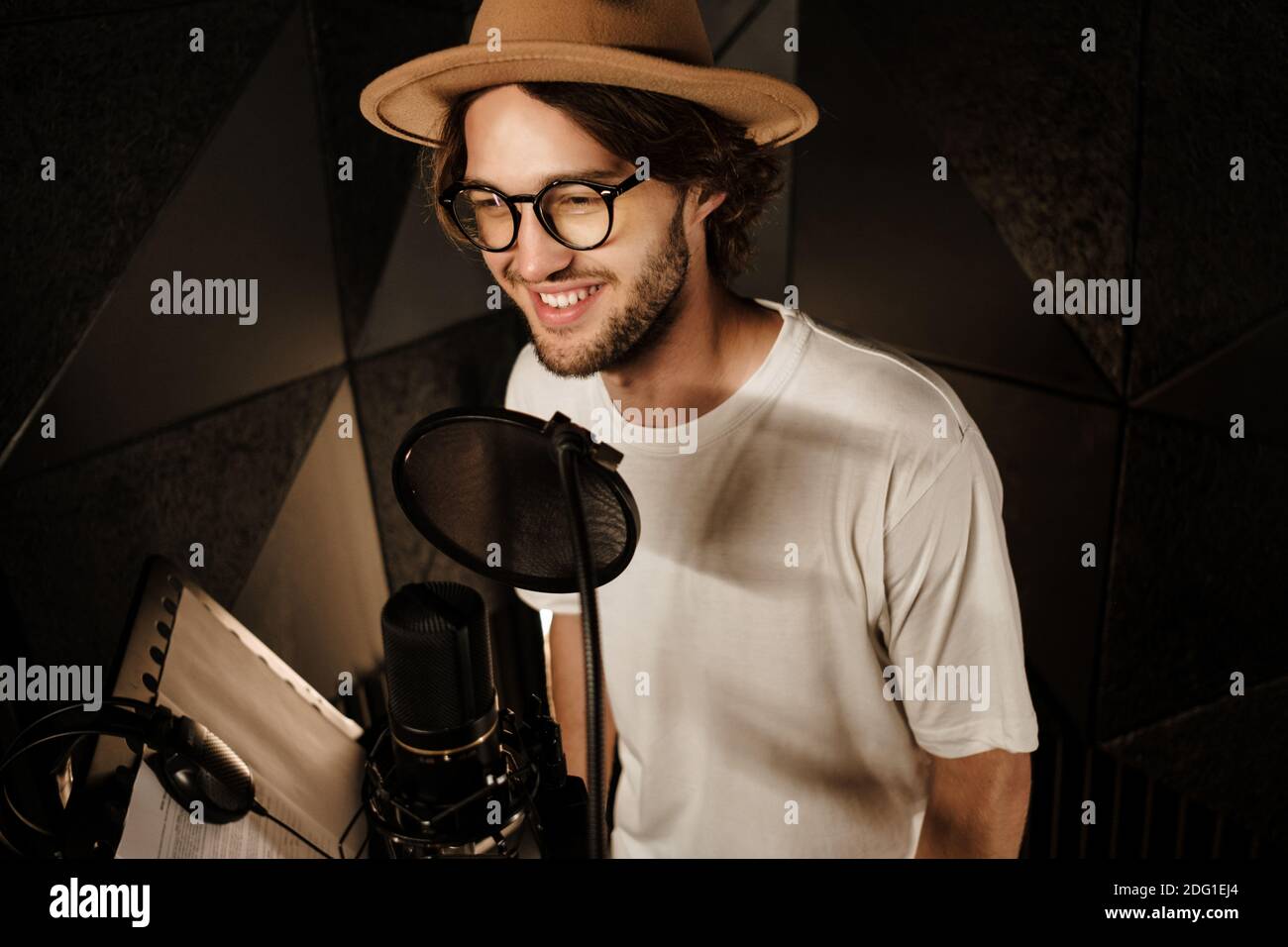 Schöner lächelnder männlicher Sänger, der gerne neue Lieder für Musik aufzeichnete Album im modernen Studio Stockfoto