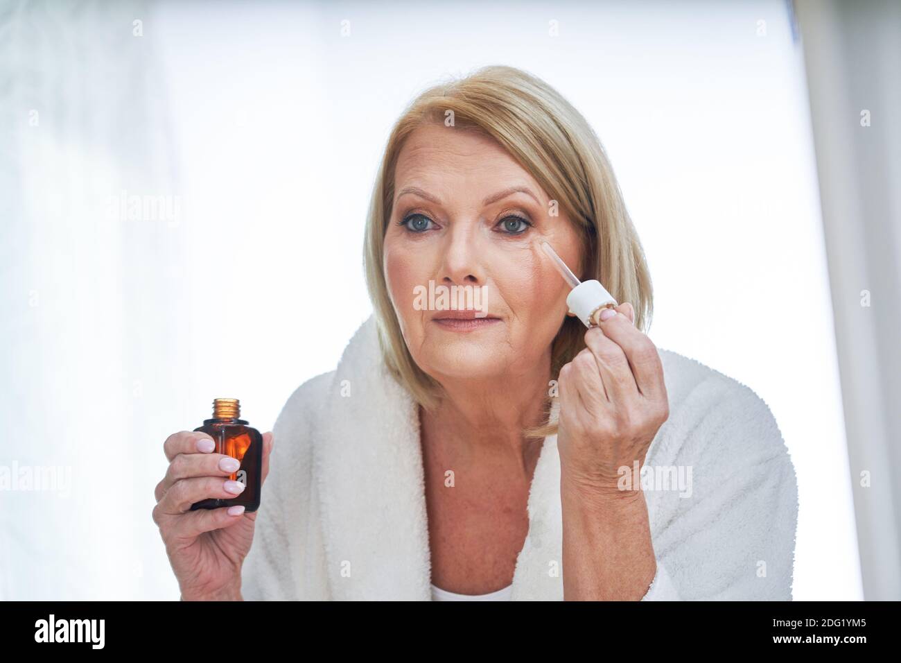 Ältere Frau mit Anti-Falten-Serum im Badezimmer Stockfoto