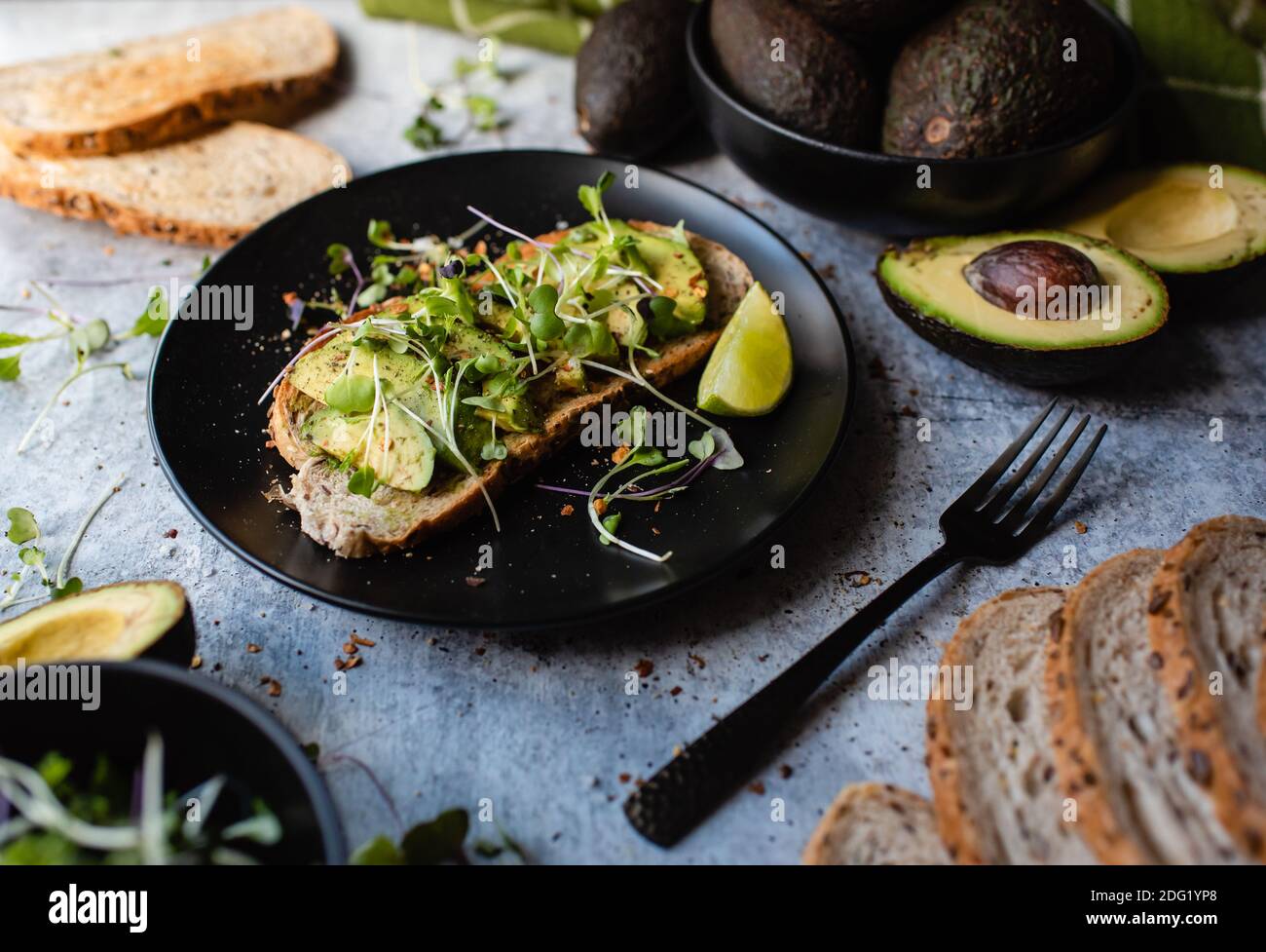 Avocado Toast auf einem Teller mit Zutaten um ihn herum auf Stein Zähler. Stockfoto