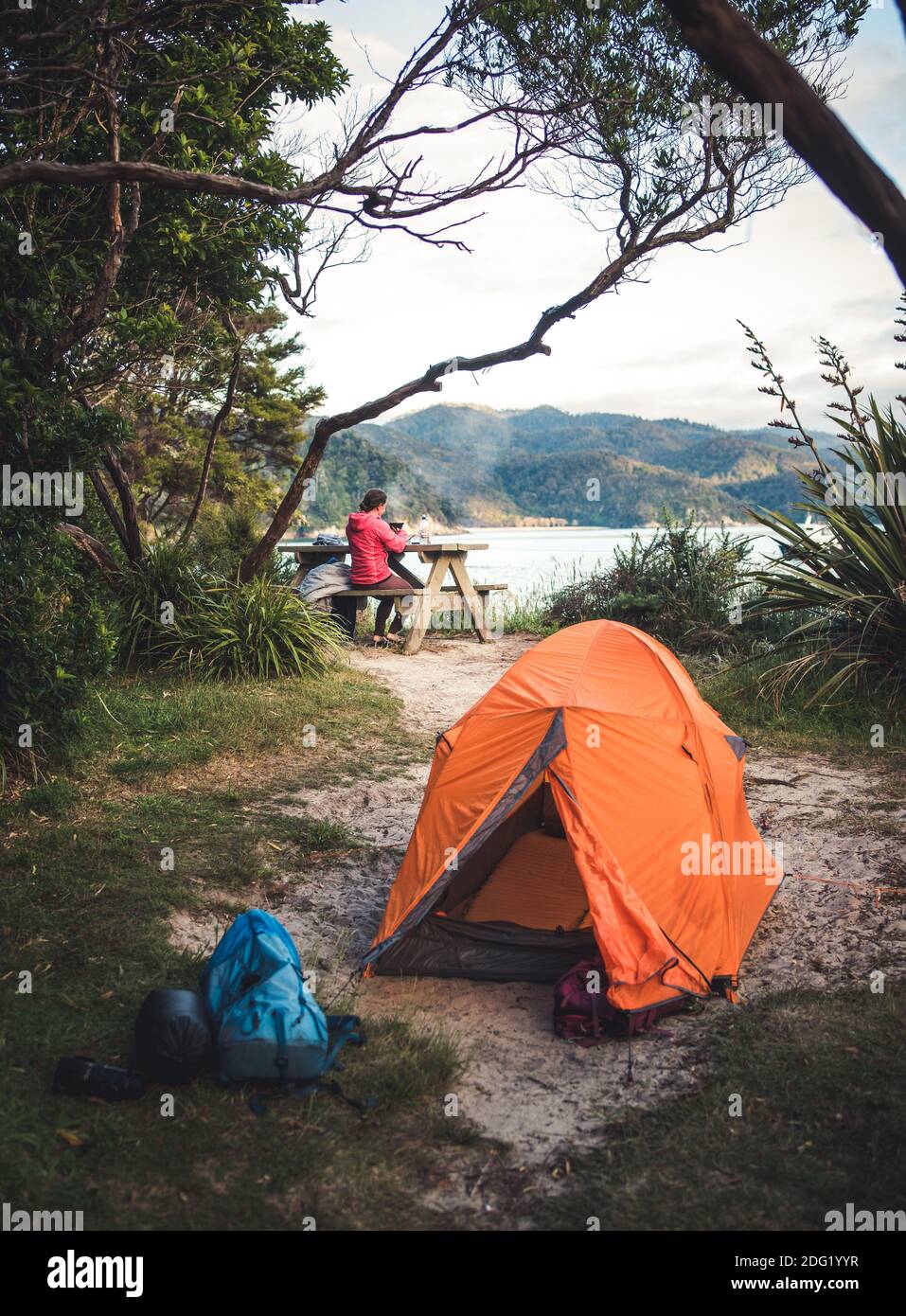 Oranges Zelt auf dem Campingplatz mit Frau, die im Hintergrund Kaffee macht Stockfoto