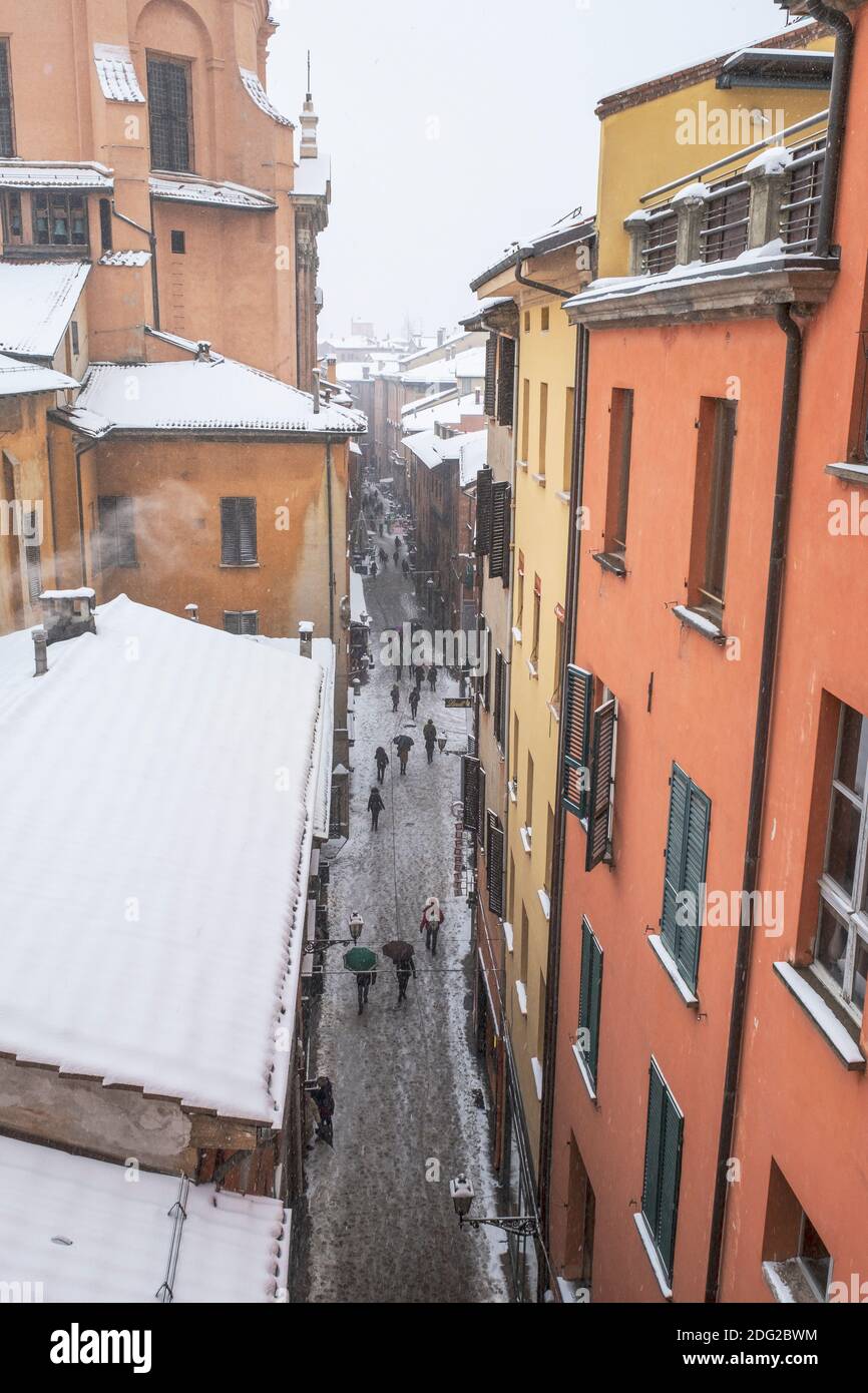 Vogelperspektive auf Menschen, die in einer engen Straße mit Schnee fallen auf bunte Häuser und Dächer in der Altstadt von Bologna, Italien Stockfoto