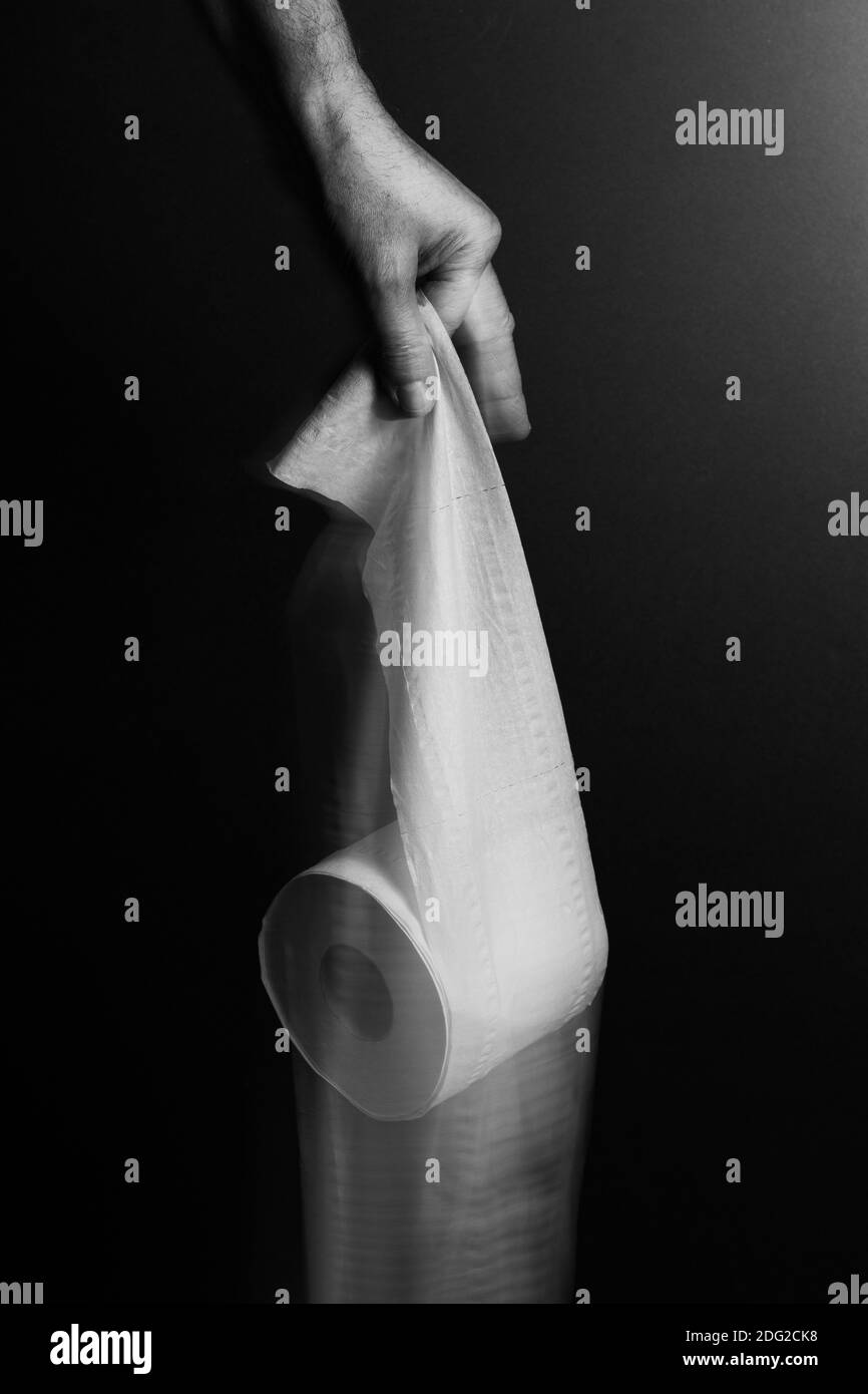 Schwarz-Weiß-Bild von einzelnen männlichen Hand fallen Toilettenrolle, mit verschwommener Bewegung, vor dramatischen dunklen Hintergrund und Beleuchtung gesetzt Stockfoto