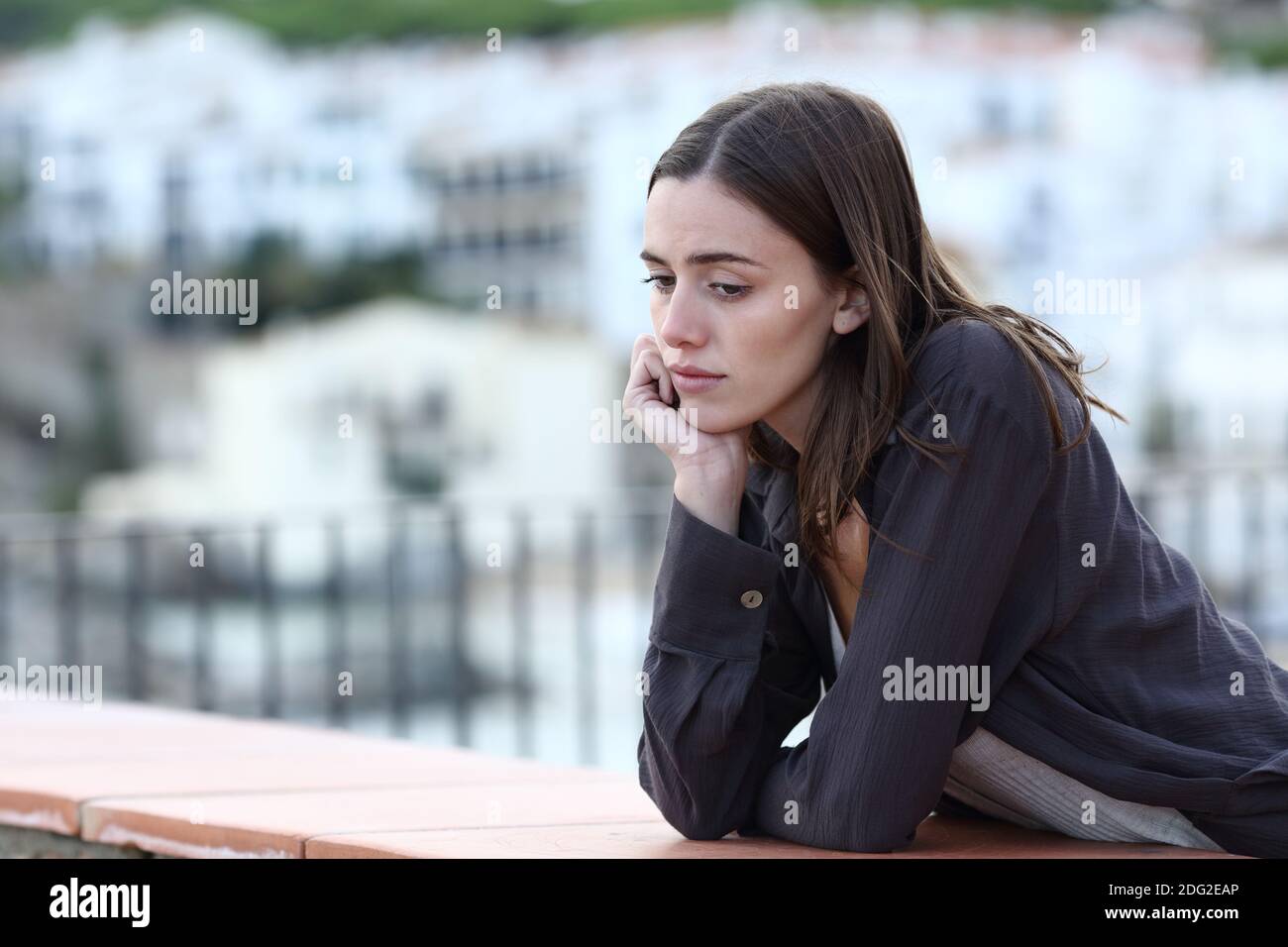 Traurige Frau, die sich beschwert hat, als sie auf einem Balkon in einem hinunterschaute Stadt Stockfoto