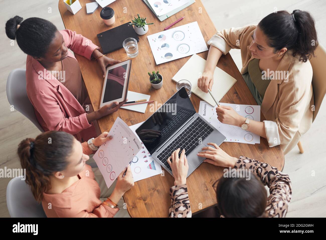 Draufsicht auf Gruppe von Frauen, die am hölzernen Besprechungstisch mit Diagrammen und Grafiken sitzen, während sie Geschäftsprojekt diskutieren, Platz kopieren Stockfoto