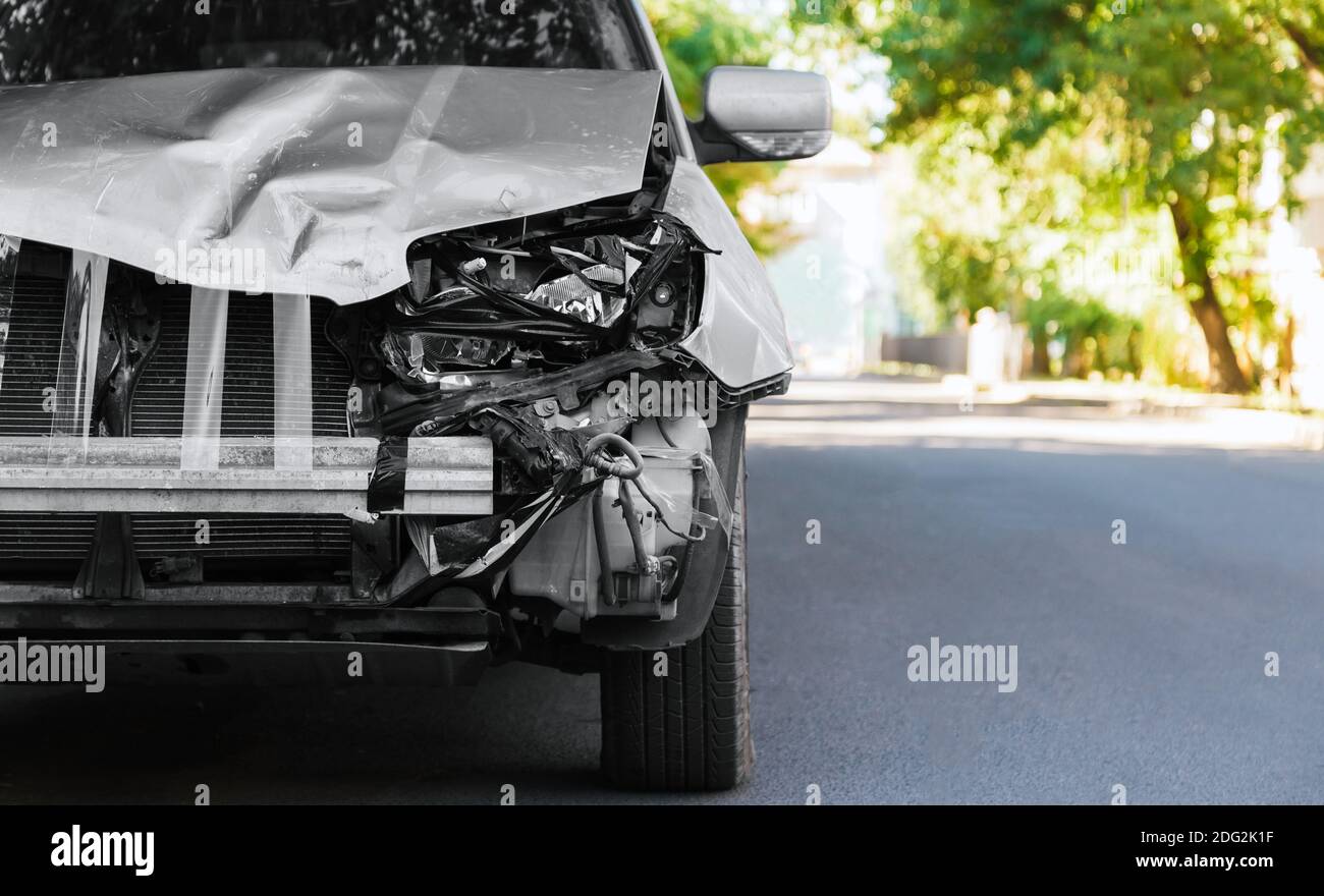 Zerstörte Auto in Autounfall Verkehrsunfall auf der Stadtstraße. Zertrümmerte kaputte Autoscheinwerfer, verbeulte Haube ohne Stoßstange in grauem Autounfall mit Kopie Stockfoto