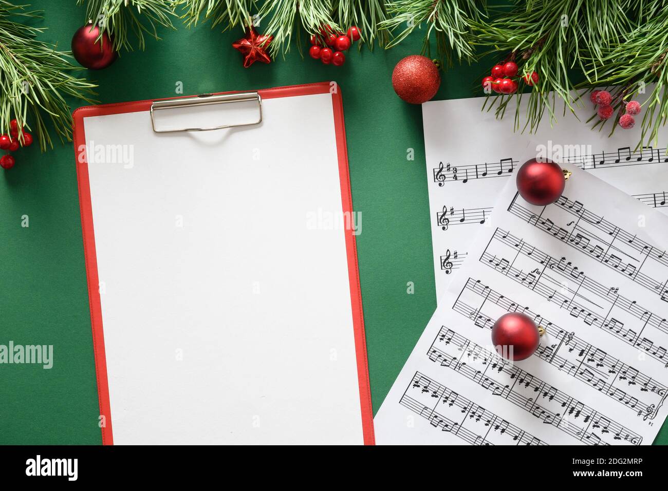 Musik leerer Rahmen für Weihnachtslieder und singt verzierte rote Kugeln auf grünem Hintergrund. Blick von oben. Leerzeichen für Text. Stockfoto
