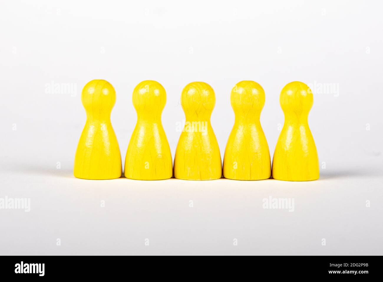 Fünf gelbe Holzfiguren in einer Reihe auf weißem Hintergrund, gruppiert Stockfoto