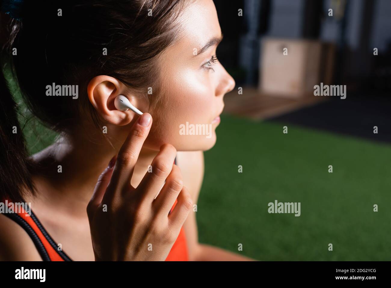 Junge Sportlerin, die schnurlose Kopfhörer anfasst und beim Sport wegschaut Zentrieren Stockfoto