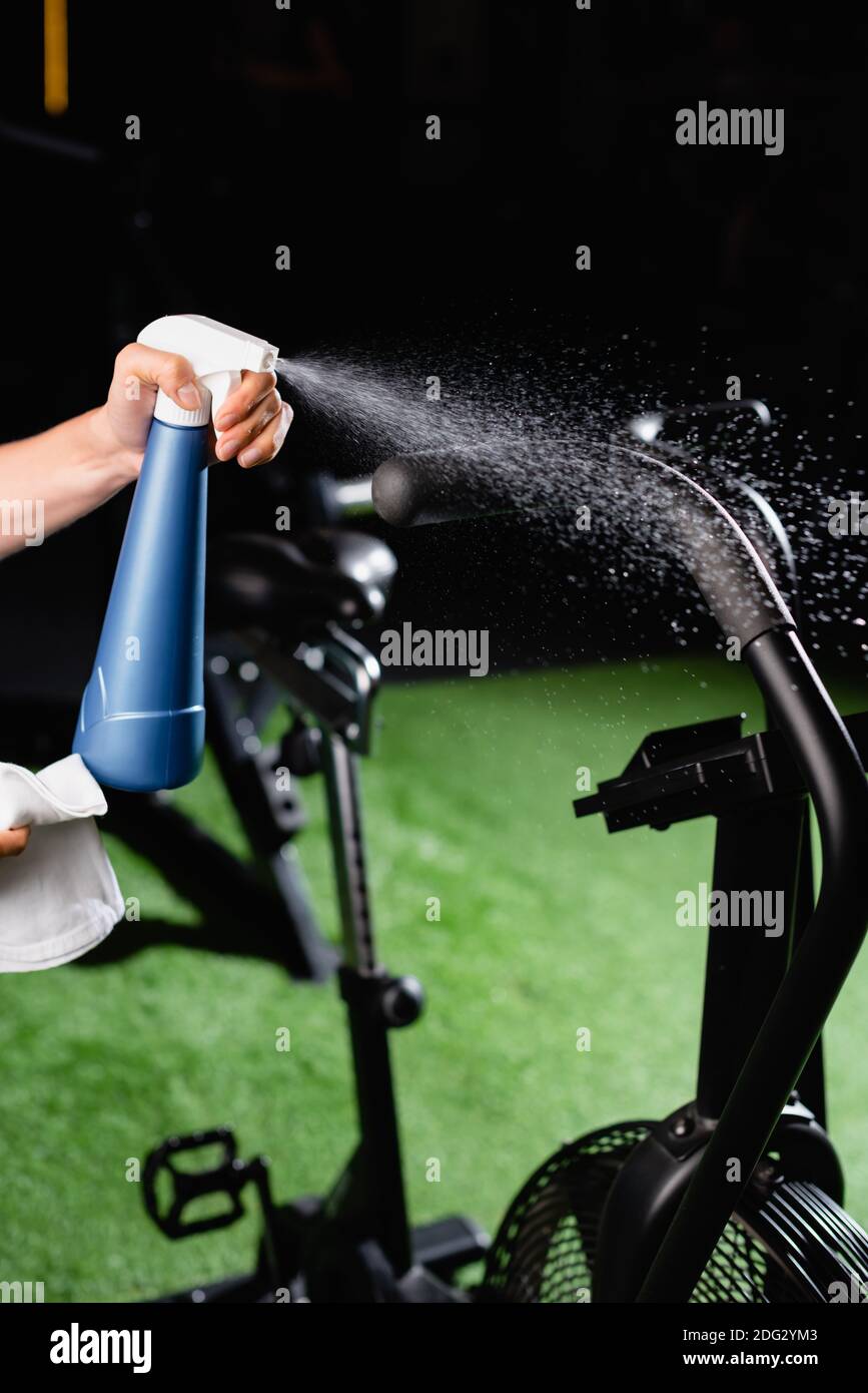 Teilansicht von Charwoman Sprühen Reinigungsmittel auf Sportgeräte in Fitnessraum Stockfoto