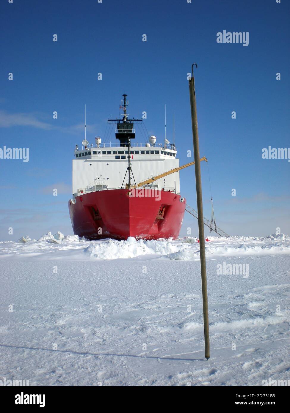 Arctic native Ice Test Stick. Ein Alaskas nativer Eisteststab, genannt "unghaq", kann im Vordergrund aus dem Eis herausragen, während der Eisbrecher Healy der US-Küstenwache im Hintergrund ist. Der Haken, der oben auf dem Stock sichtbar ist, dient zum Auffinden von Dingen, wie zum Beispiel das Greifen der Kleidung einer Person, wenn sie ins Wasser fallen, und das andere Ende wird zum Stocken des Eises verwendet. Unghaqs sind ein hoch geschätztes Sicherheitsinstrument für Alasker, die in Küstengemeinden leben und sich im Winter auf das Eis wagen, um dort zu jagen. Stockfoto