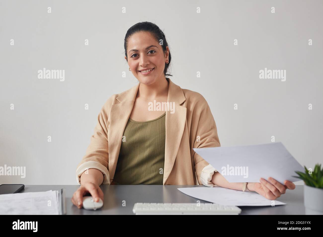 Porträt einer jungen Frau mit gemischtem Rennen, die lächelt, während sie am Schreibtisch den PC benutzt, Online-Meeting-Konzept, POV Stockfoto