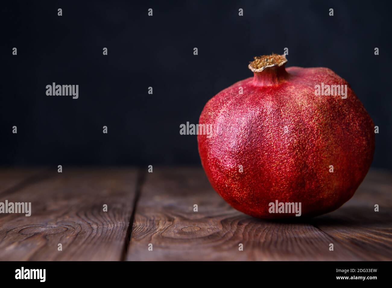 Reifer saftiger Granatapfel liegt auf einem braunen Holzhintergrund. Granatapfelsaft gegen Coronavirus. Stockfoto