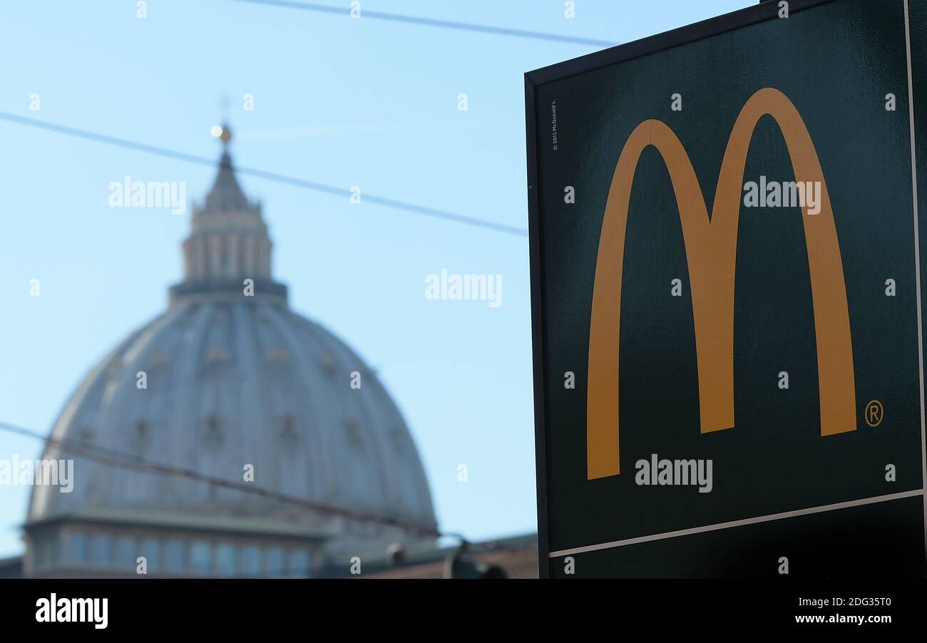 Ein Schild, das die Richtung eines neu eröffneten McDonald's Restaurants zeigt, ist am 4. Januar 2017 in Rom, Italien, mit der Kuppel der Petersbasilika im Hintergrund in der Nähe des Vatikans zu sehen. Die amerikanische Fast-Food-Kette eröffnete ein Restaurant in einem Gebäude im Besitz des Vatikans, trotz des Protests eines Komitees zum Schutz von Borgo, dem historischen Viertel rund um den Vatikan, in dem viele Kardinäle leben. Trotz einer sehr öffentlichen Schlacht von Einheimischen und religiösen Beamten, um die Fast-Food-Kette aus dem päpstlichen Hauptquartier zu halten, öffnete eine Filiale der Golden Arches Kette Restaurant für Geschäfte nur wenige Meter entfernt Fr. Stockfoto