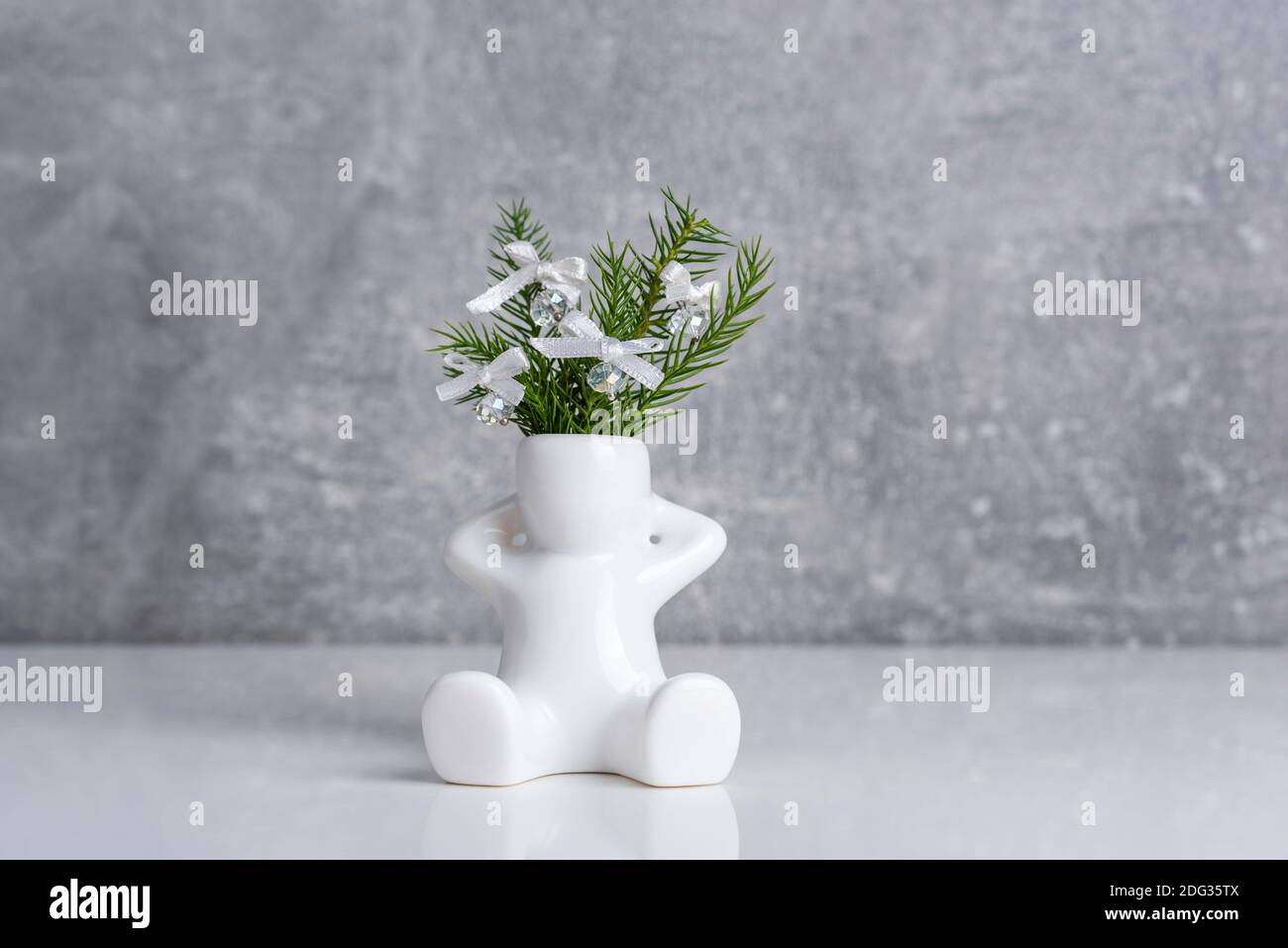 Kleine weiße Keramikvase - Figur des Menschen mit Araucaria Pflanzenzweige mit Glasperlen und Band Bögen verziert. Miniatur-Weihnachtsdesign. Stockfoto