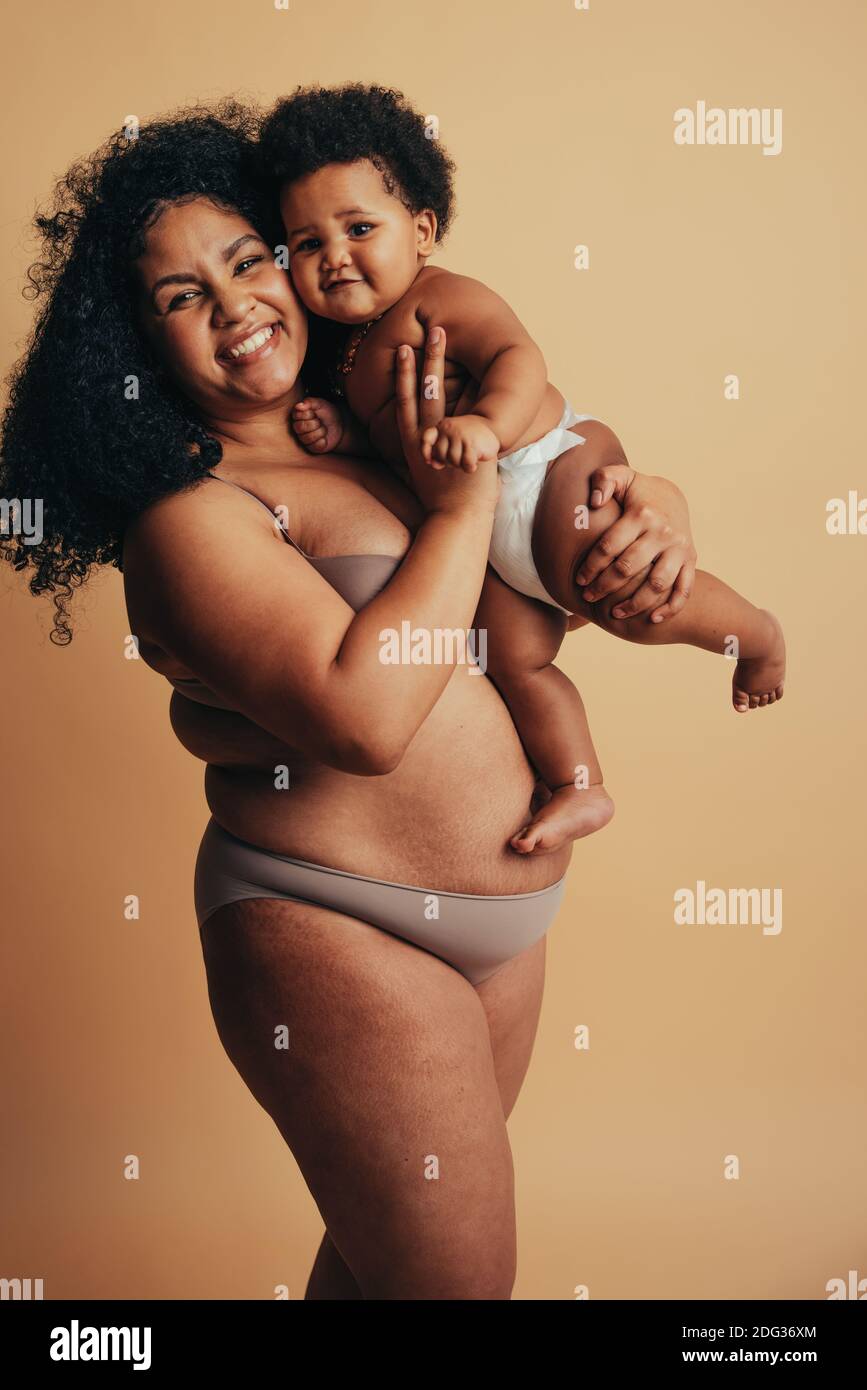 Plus size Frau hält ihr Baby auf. Starker Körper positive Frau postpartum. Echter Körper einer gesunden Mutter. Stockfoto