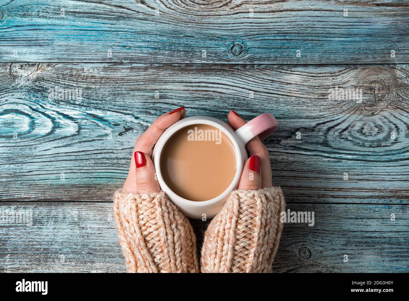 Damenhänden halten eine runde Keramikschale mit einem heißen Kaffeegetränk auf einem hölzernen Hintergrund. Stockfoto