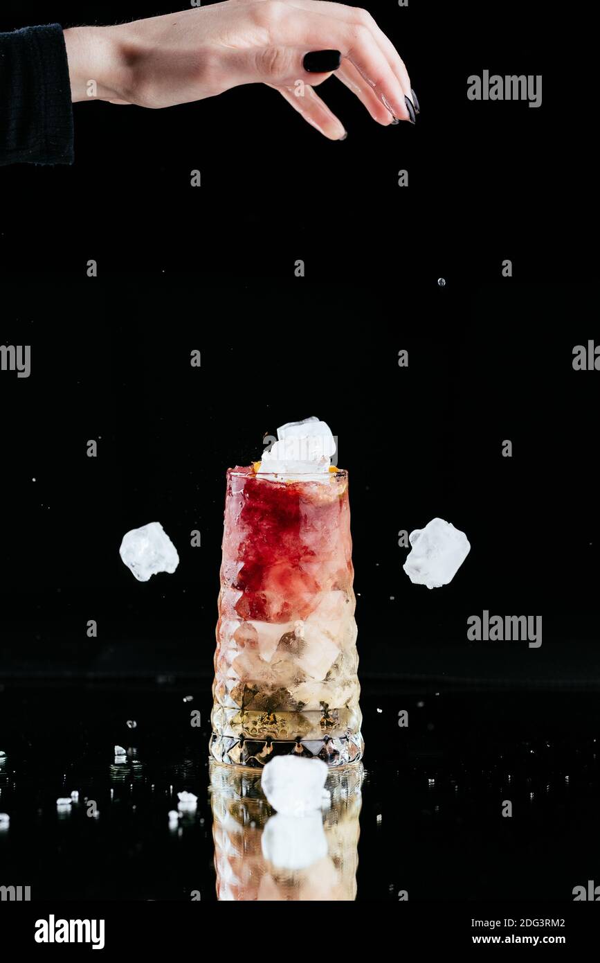 Heller alkoholischer Cocktail auf schwarzem Hintergrund und einer Frau Hand mit fallendem Eis Stockfoto