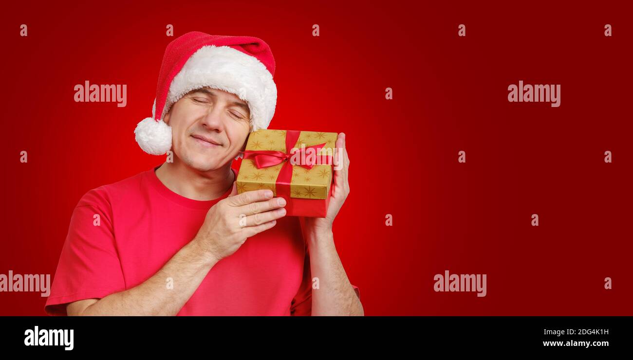 Mann in Santa Hut erhalten Weihnachtsgeschenk, hält in der Nähe seines Gesichts und lächelnd Stockfoto