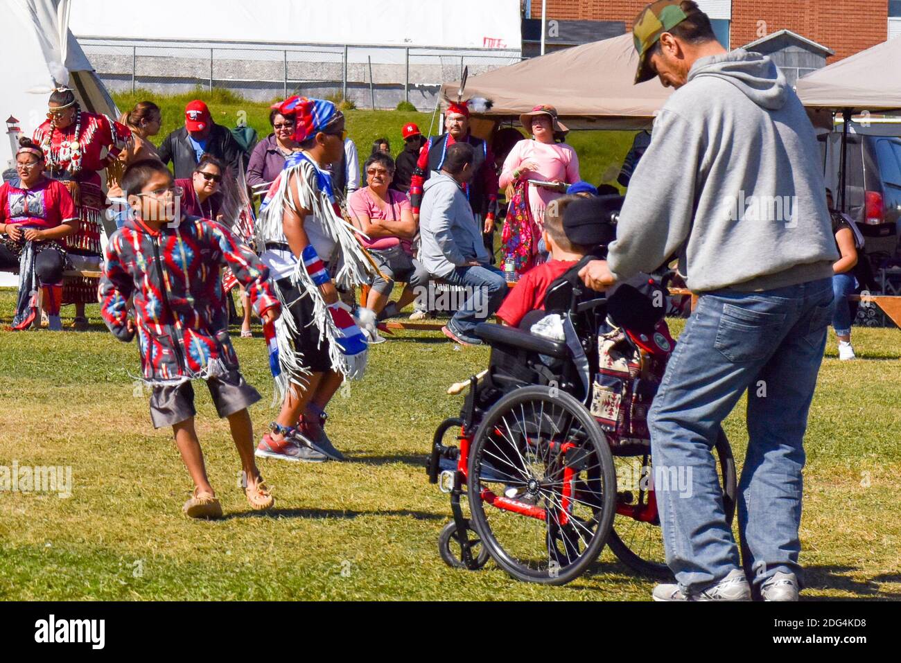 Eingeborener Vater hilft seinem Sohn auf einem Rollstuhl, Spaß zu haben und zu tanzen während einer Pow Wow Veranstaltung, Nord-Quebec, Kanada Stockfoto