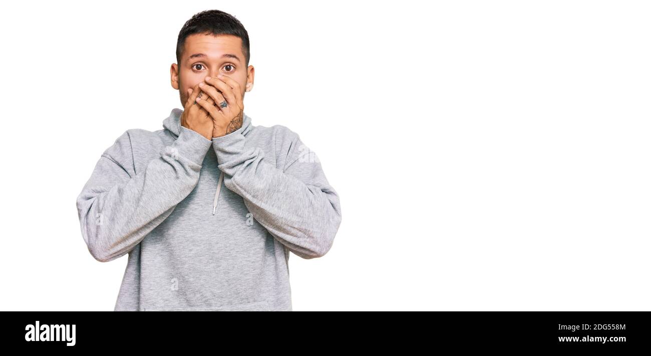 Schöner Mann mit Tätowierungen tragen lässige Sweatshirt schockiert Abdeckung Mund mit Händen für Fehler. Secret Konzept. Stockfoto