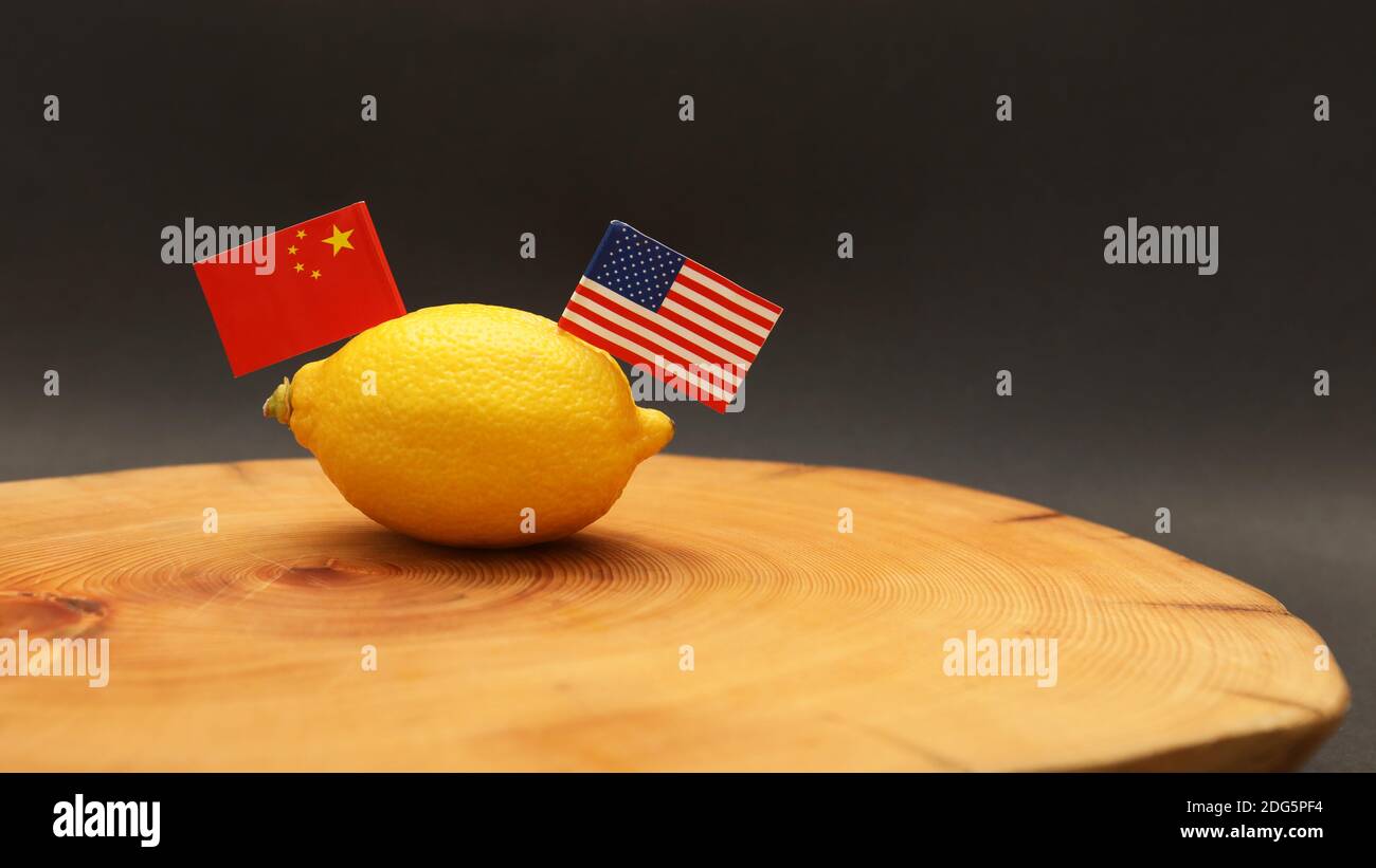 US-amerikanische und chinesische Flaggen, die aus einer Zitrone stossen Auf einem Hackblock, der die angespannte seelengeruhter Beziehung und darstellt Zwischen den Handelskriegen wird ein Handelskrieg geführt Stockfoto