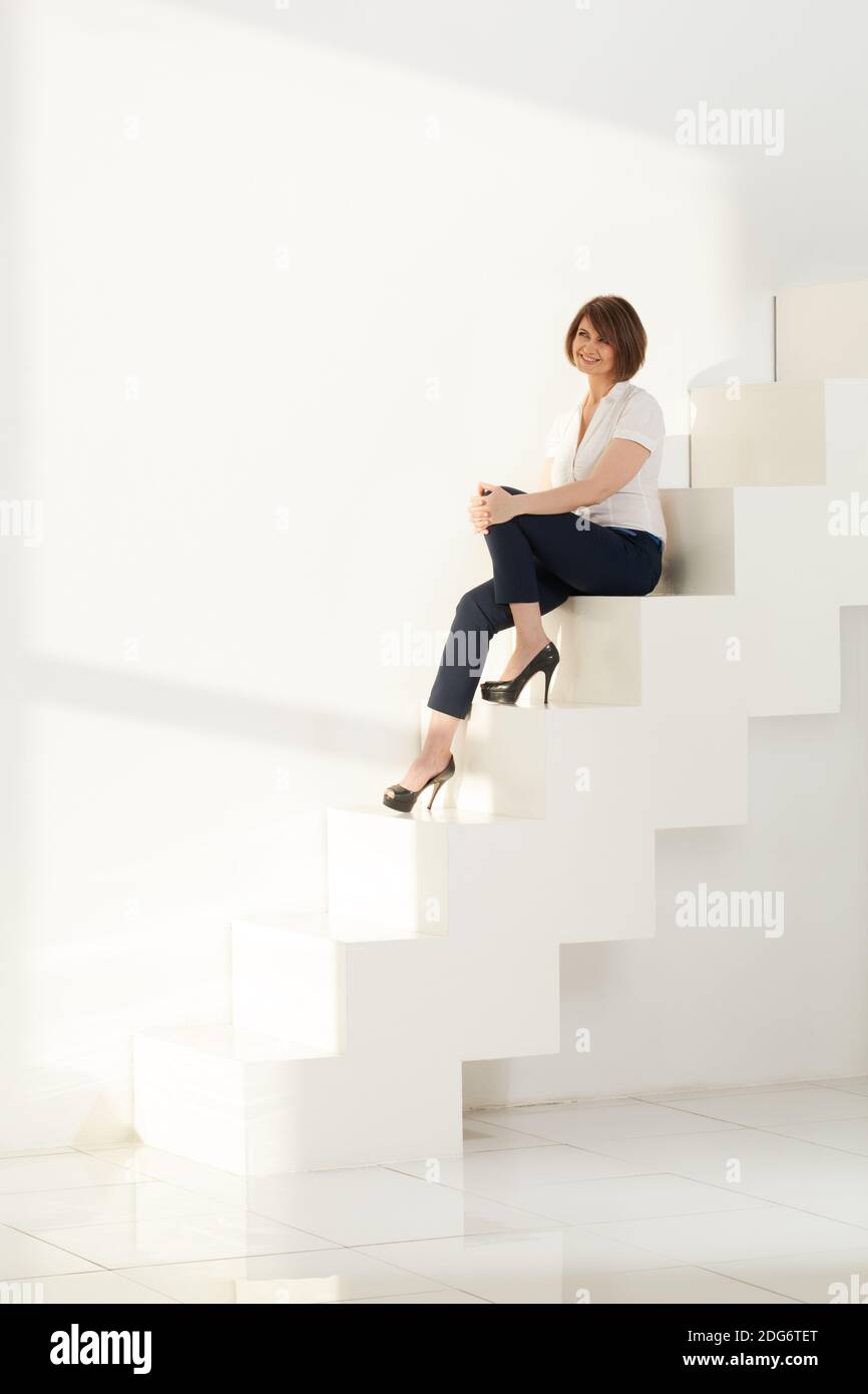 Elegante Erwachsene Frau sitzend auf Schritte lächelnd Stockfoto