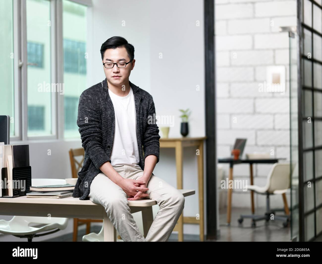 Porträt eines jungen asiatischen Geschäftsmannes, der im Büro auf dem Schreibtisch sitzt Blick nach unten Stockfoto
