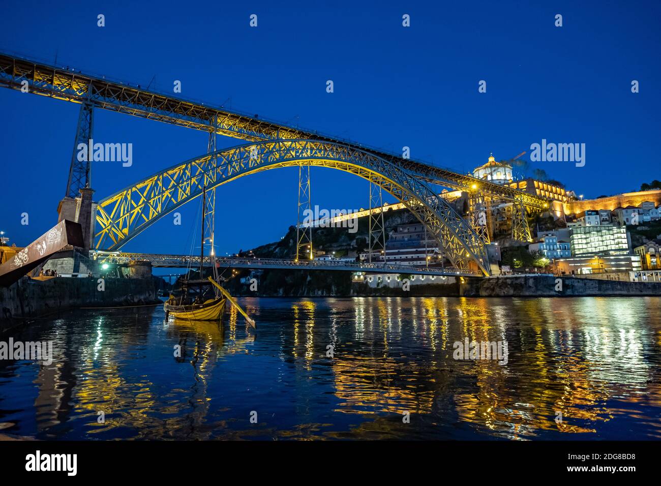 Niedriger Weitwinkelclip der Luis I Brücke bei Abenddämmerung in Porto, Portugal. Holzrabelo Boot im Vordergrund Stockfoto